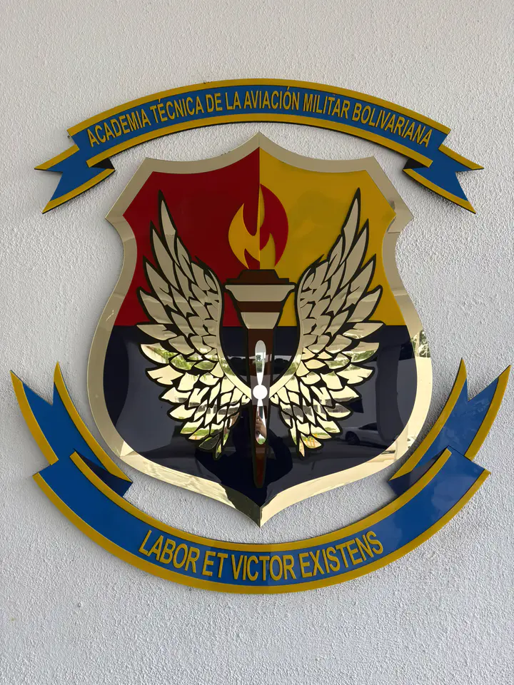 Escudo de la academia en la pared, con la antorcha, las alas doradas, la hélice y las cintas con su nombre
